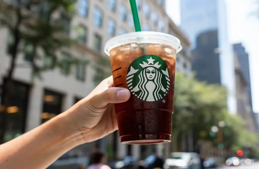 Hand holding a Starbucks iced Americano with no sugar or cream in a city setting.