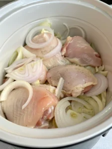 Raw chicken thighs layered over onions in crock pot